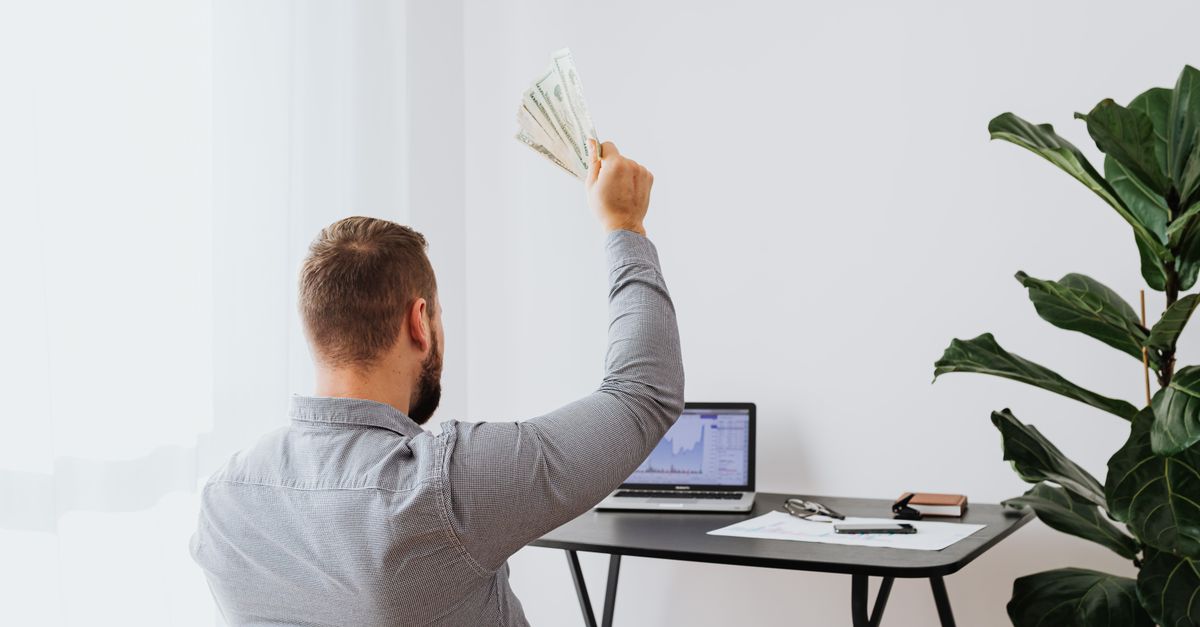 A man in a home office raises cash, symbolizing financial success and achievement.